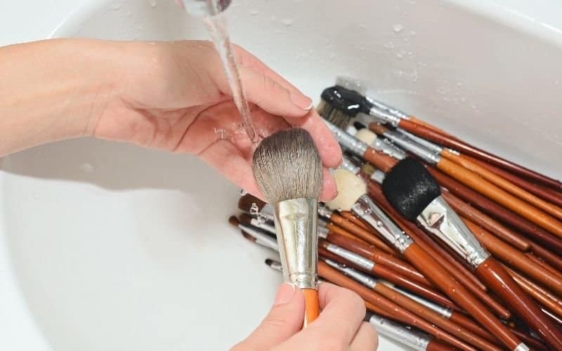 a pair of hand cleaning the makeup brushes on running water