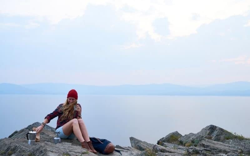 a woman having a picnic alone on a large rock overlooking the sea.