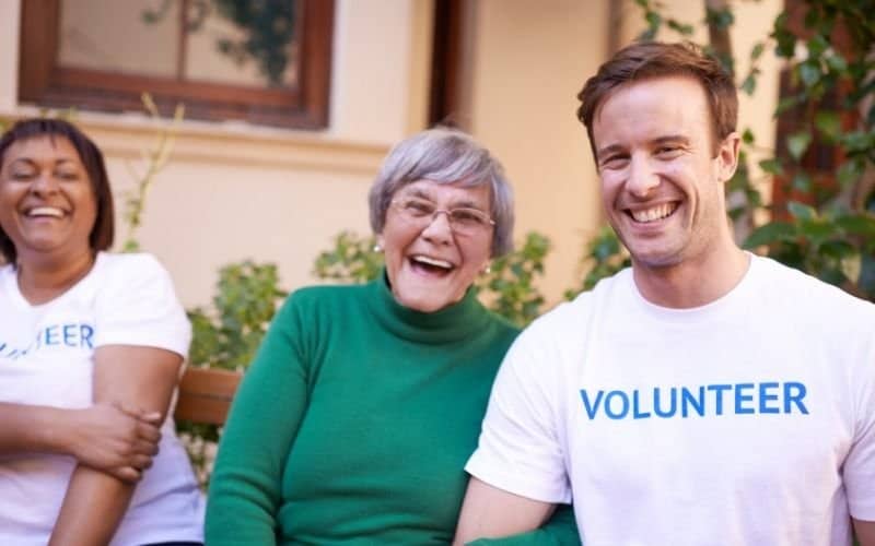 photo of three person with a man wearing a white t shirt with a word volunteer on it