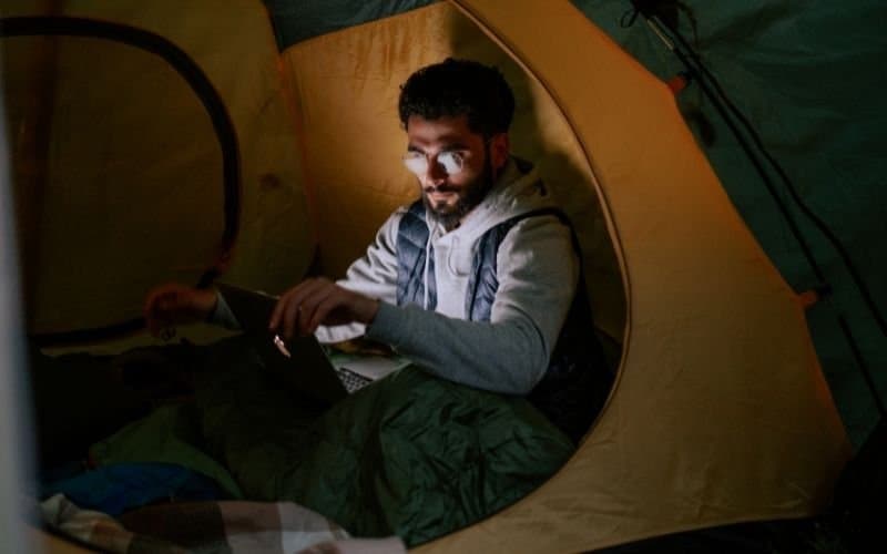 a man sitting with his laptop in a tent