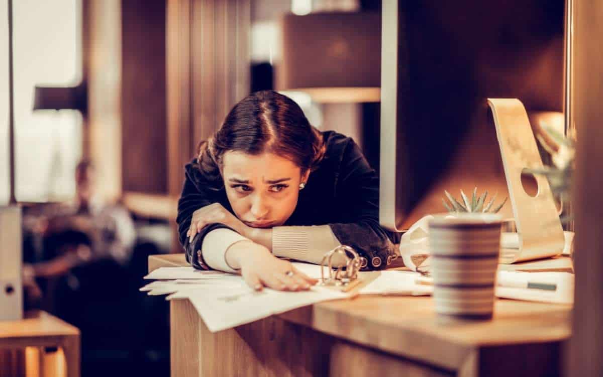 A woman slouching on the table with her upper body over some papers with a coffee mug i front of her