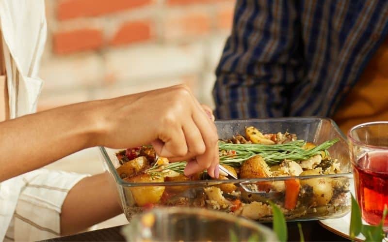 Image showing hand picking on the foods from a glass container with drinking glasses and another person nearby