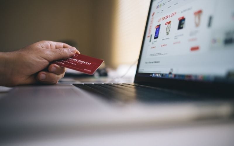 Image showing a hand holding a credit card in front of a laptop that shows a shopping website