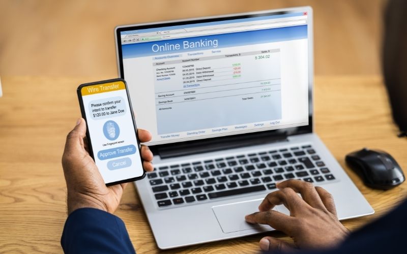 Photo of two hands of a man while doing an online money transfer using mobile phone and a laptop