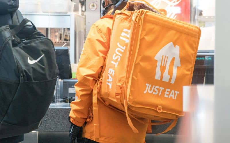 A man wearing yellow jacket with yellow backpack with printed word Just eat