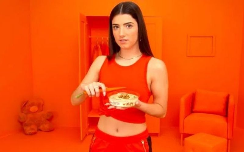 Photo of a young woman in orange clothes holding food in orange background