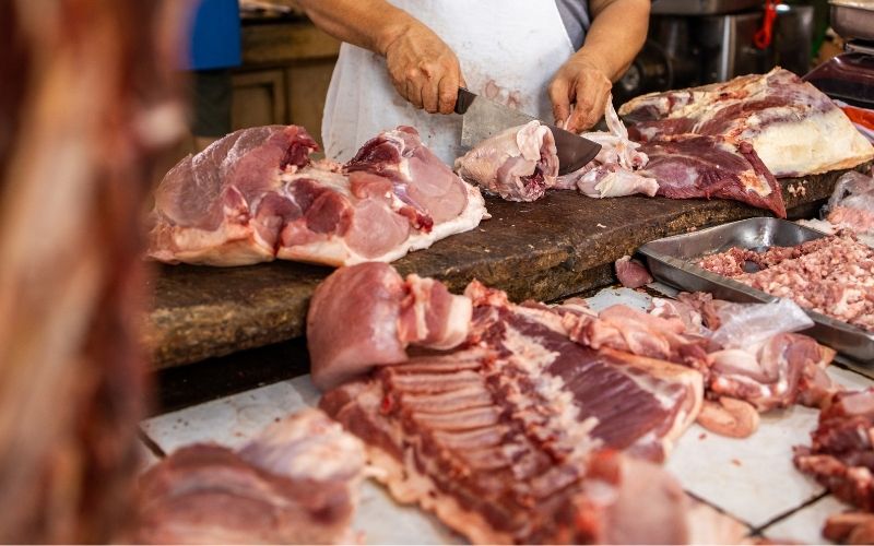 Photo of a man with a knife slicing a piece of meat in front of several more meats