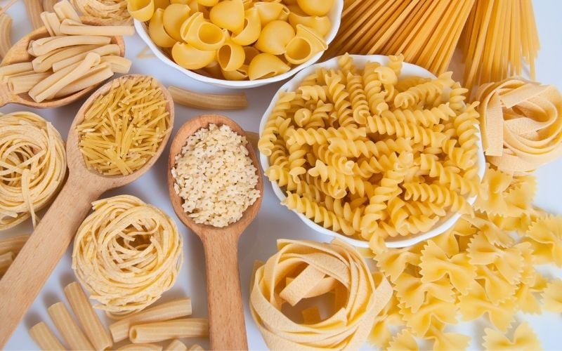 Photo of different uncook pasta in bowls and wooden spoons