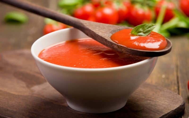 Photo of a white bowl filled with tomato sauce and a wooden spoon with tomato sauce