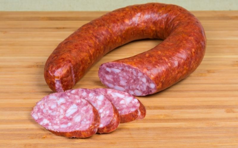 Photo of a bologna sausage with three slices on a wooden chopping board