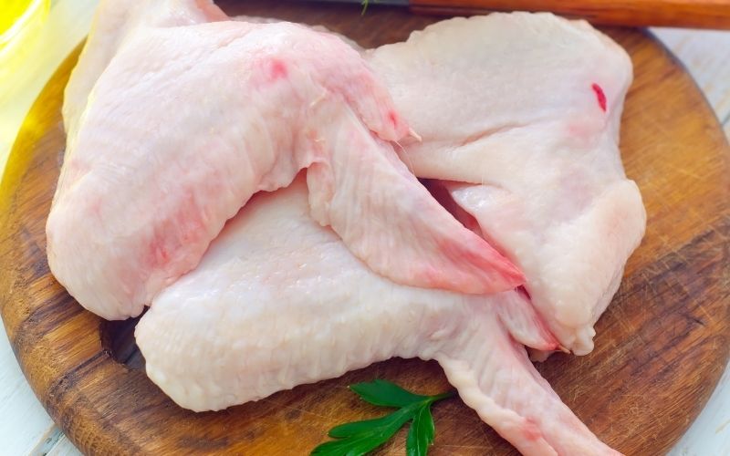 Photo of fresh cuts of chicken wings on a wooden chopping board