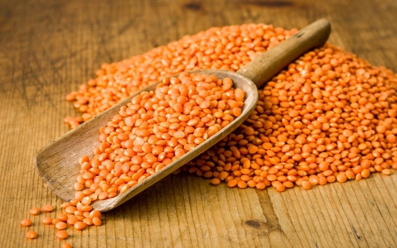 Photo of red lentils on a wooden scoop on a wooden board