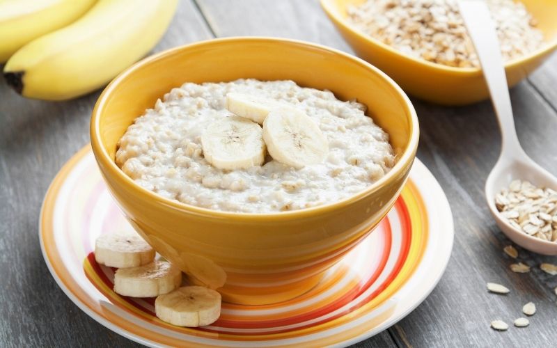 Photo of a cooked oatmeal with sliced banana placed in a yellow bowl on a saucer