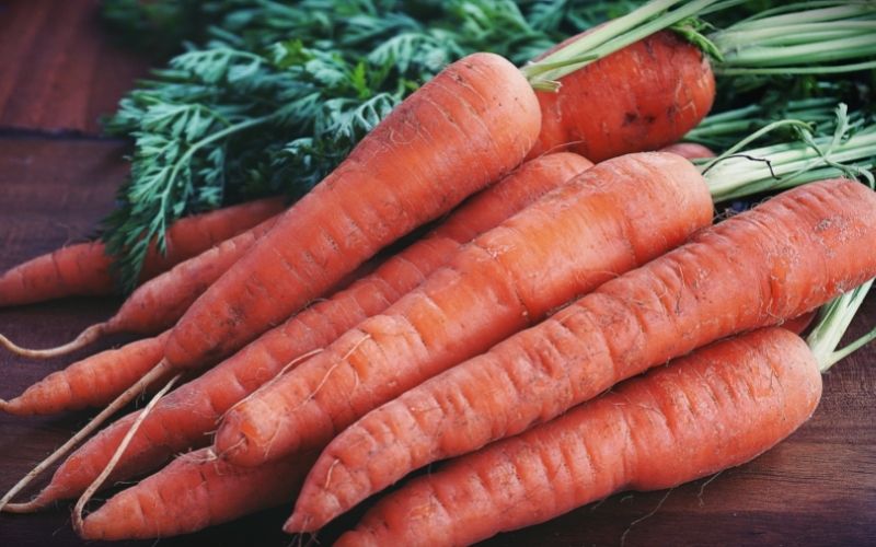 Photo of several carrots with some green vegetables beside them