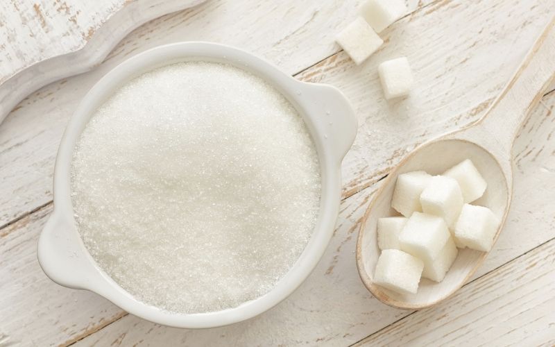 photo of granulated sugar in white bowl and cubed sugar in white wooden spoon