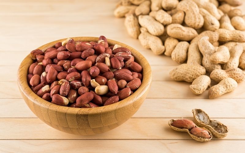 Photo of peanuts in a wooden bowls with some peanuts in shell nearby