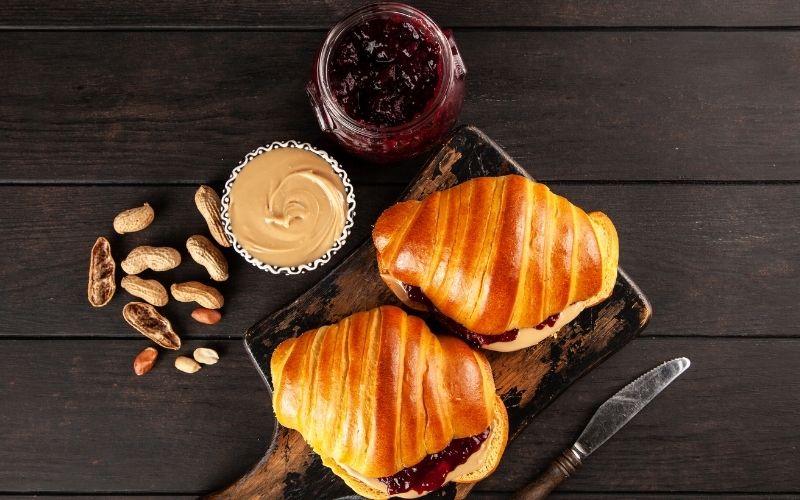 Photo of peanut butter and jelly spreads in jar next to two breads in top view