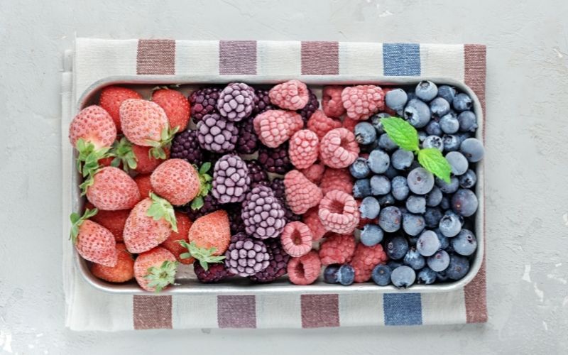 A top view photo of several kinds of frozen berries in a container