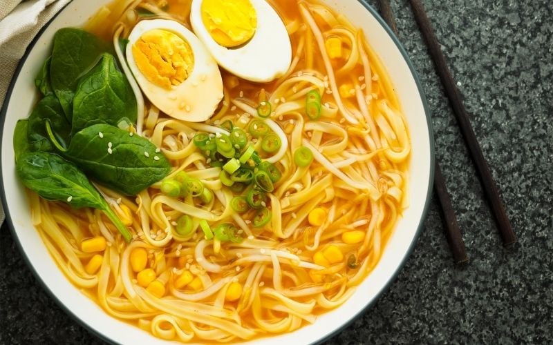 Photo of cooked ramen noodles with sliced boiled egg and vegetables in white bowl