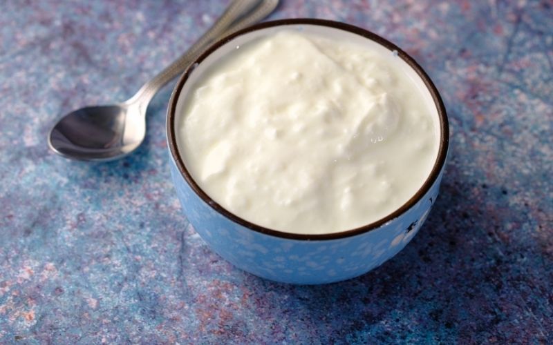 Photo of a blue bowl filled with fresh yogurt with a teaspoon beside 