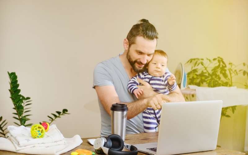 Man Working at Home with a Laptop with a Baby on His Hands