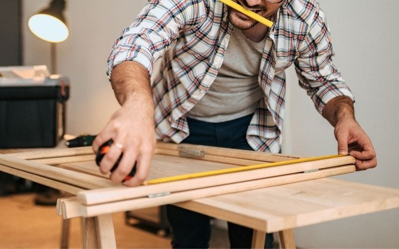 Pho of a man measuring a wood on a wooden table