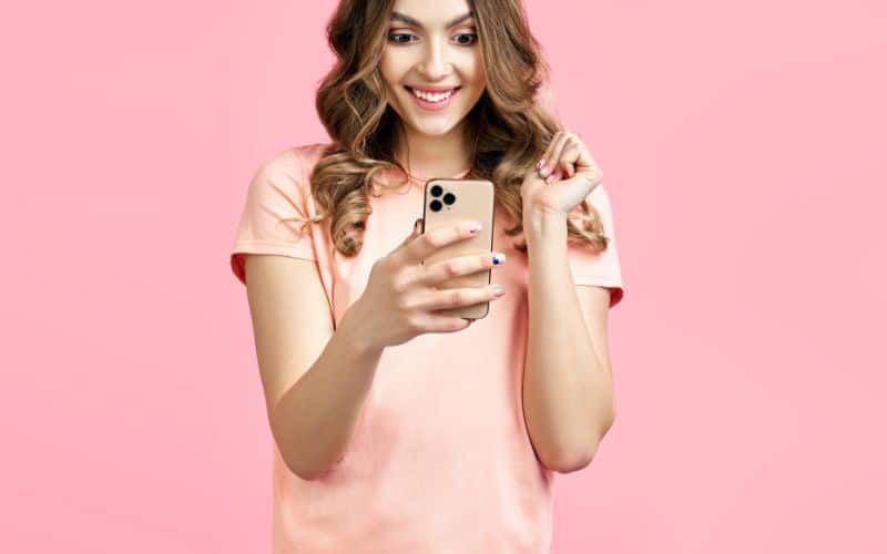 A woman holding her cellphone while looking at it happily