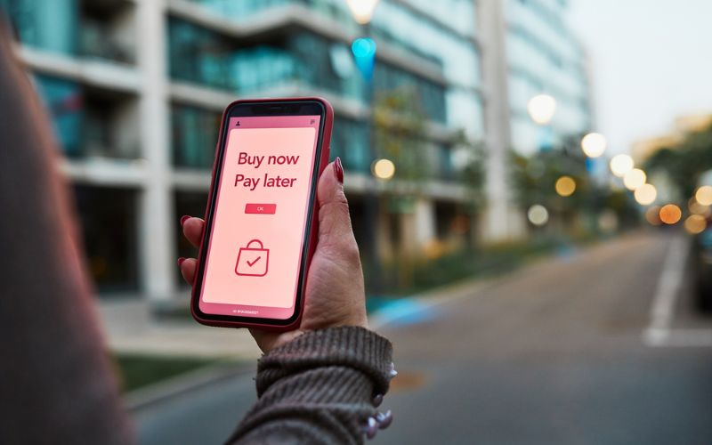 A hand holding a phone showing an app that reads Buy now pay later