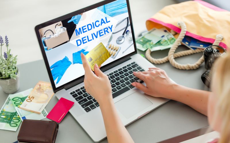 A hand holding a credit card while the other hand typing on a laptop that shows medical delivery website