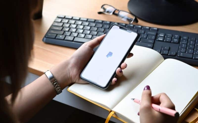 Image showing a hand holding a smart phone with an apple app over a notebook beside a keyboard