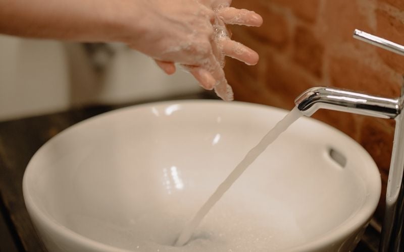 Photo of a pair of hands with lather over a white sink with running water from the faucet