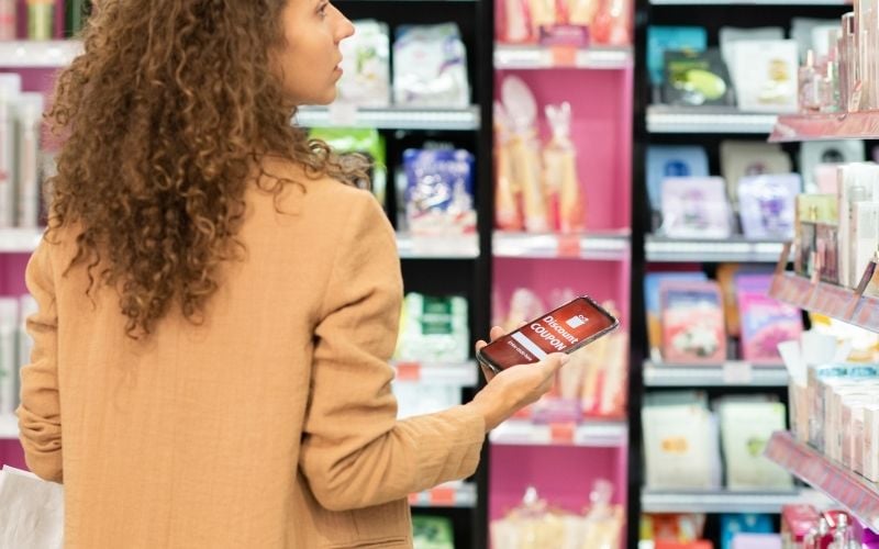 Photo of a woman holding a mobile phone while looking at the products on the shelves