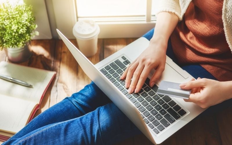 Photo of a woman sitting with a laptop on her lap while holding a card