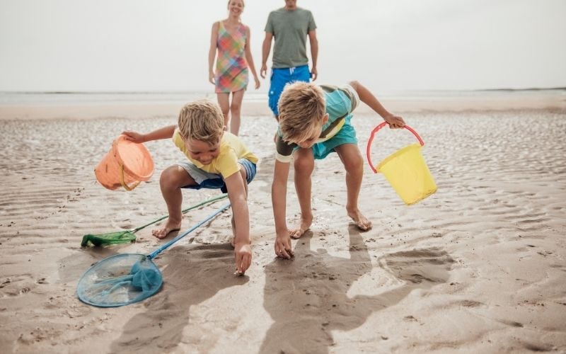 Photo of two children playing on the sand with adult man and woman behind them