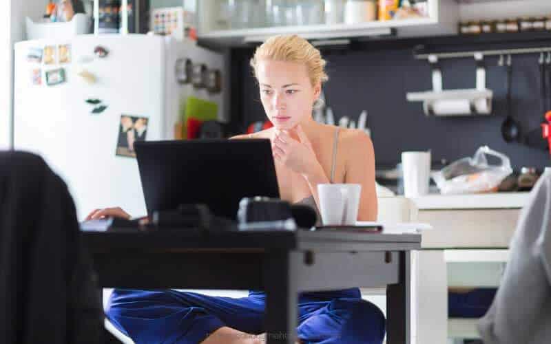 Woman in the kitchen sitting with laptop in front of her_Ways to Make Extra Money in the UK