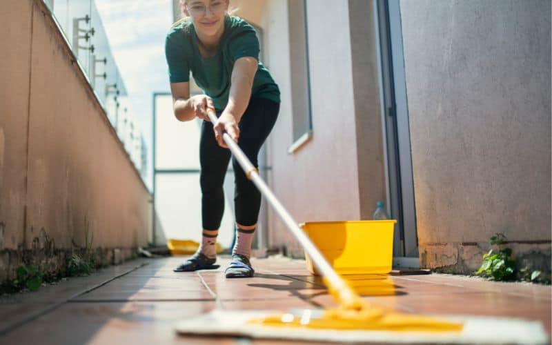 A young person holding a mop and cleanig the floor with yellow bucket beside her to make some money