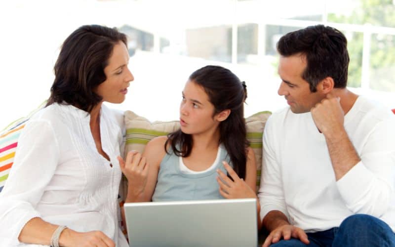 A couple with a young woman discussing in front of the laptop while sitting in the sofa