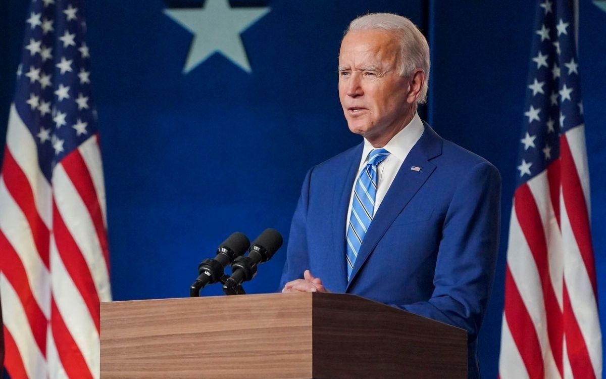 Photo of US President Joe Biden speaking while standing with US flags behind him