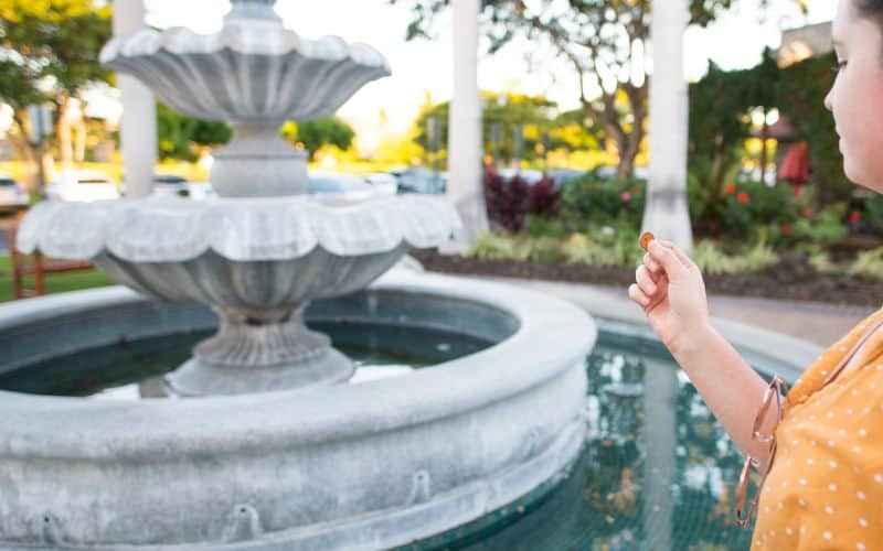 Photo of a woman holding a coin in front of a fountain