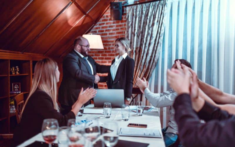 Photo showing people around a table with one person congratulating another person