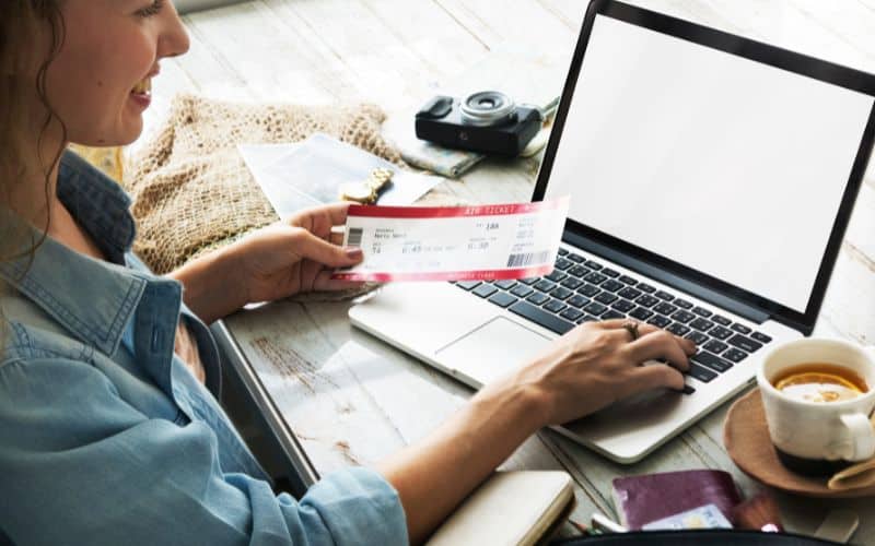 Photo showing a person in front of a laptop while holding a travel ticket