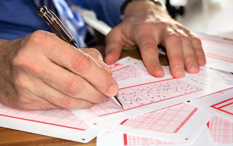 Photo showing a pair of hand over some lottery tickects while one hand is writing on it