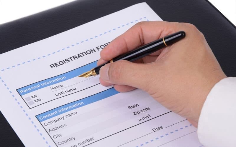 A hand holding a pen over a registration form.