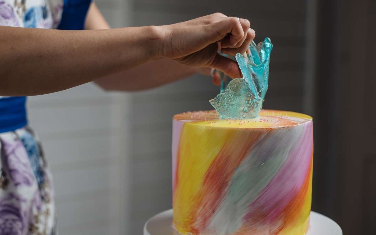 A pair of hand holding a cake decoration on top of a colorful cake made made from home