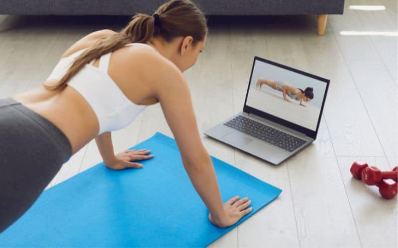 Woman excercising at home while watching a coach on a laptop in front_Ways to Live a Rich Life on a Tiny Budget