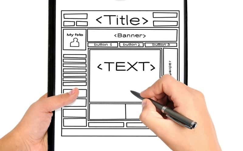 Image showing a plan for the website with words that read Title and Text, with a hand holding a pen and another hand holding the board with the design plan.