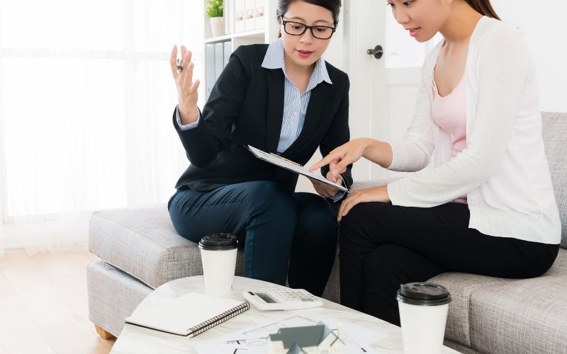 Photo of two women sitting and discussing something with papers and cups on a table in front of them